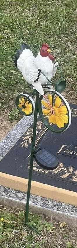 A ceramic chicken on a metal bicycle ornament at a grave