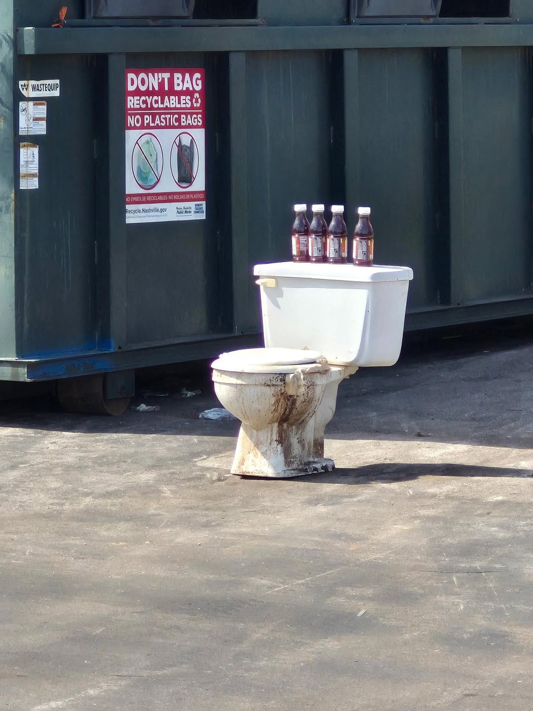 A toilet in a parking lot with bottles on top